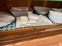 White porcelain serveware on shelf: baking dish, platters, gravy boat, condiment dish, large bowl, stack of shallow bowls