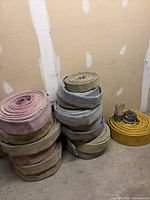 Three stacks of rolled 4" layflat fire hoses with couplings visible