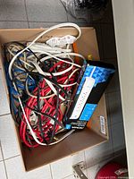 Box containing assorted red, black and white extension cords, Ethernet cables and NOMA power bar package visible