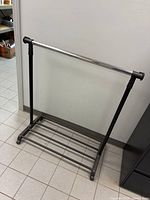 Full view of garment rack showing chrome bar, black supports, lower shelf