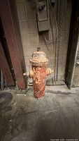 Full view of cast iron fire hydrant standing on concrete floor, showing faded orange paint and rust