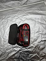 Open case displaying ES 655 clamp meter with test leads and manual