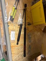 Two gas struts of different lengths and bagged ball-stud hardware on shelf