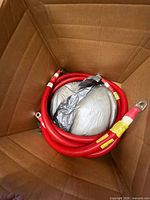Coiled red battery cable with metal lugs in shipping box