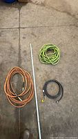 Three coiled rubber air hoses in orange, green, black with measuring stick for scale