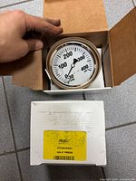 Gauge in open inner box and outer box with label visible
