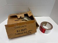 Cardboard box containing white reflective tape roll and separate red reflective tape roll
