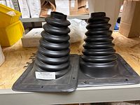 Two black rubber steering column boots on shelf, square mounting flanges visible, part label showing KME-042493V001