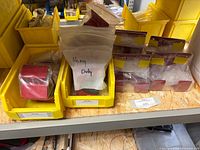 Multiple red metal brackets in yellow bins; each sealed in plastic