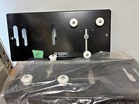 Two black steel wall mount plates with white rollers, one loose, one in packaging