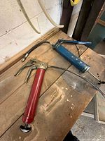 Red and blue grease guns on workbench with hoses attached