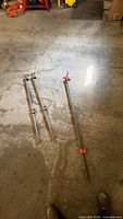 Three steel pipe clamps on concrete floor, showing relative lengths and red clamp heads