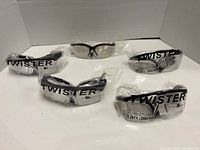 Five individually wrapped safety glasses arranged on white surface