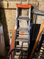 Front view of stacked aluminum step ladders showing rungs and orange tops