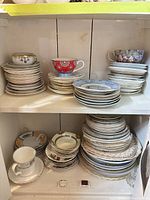 Stacked teacups, saucers and plates on two-tier cabinet shelf