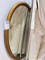 Full view of oval gold frame mirror leaning against wall