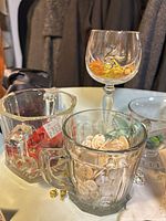 Glass mugs and goblet holding assorted buttons and ribbons