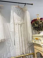 Full view of ivory lace long sleeve wedding dress with attached tulle skirt, veil and headpiece hanging on rack