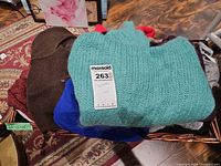 Basket with teal fuzzy sweater on top and additional folded sweaters beneath
