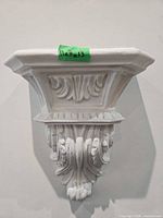 Front view of one white plaster wall corbel showing ornate fleur-de-lis and botanical relief