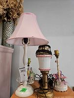 Overview showing three of the lamps including tall white lamp with pink shade, milk glass lamp with cage shade, and floral base lamp