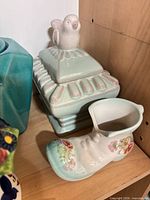 Mint green lidded jar with bird and boot planter next to it