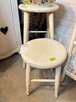 Two distressed white wooden stools, round seats, footrest rungs