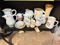 Group of assorted vintage porcelain and ceramic pitchers, creamers, vase and saucers on shelf