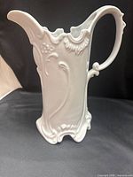 Full left-side view of ornate white porcelain pitcher showing relief decoration
