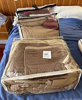 Two clear zippered bags on bed containing folded tan comforter and quilt