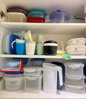 Cupboard with three shelves of plastic containers, pitcher, tumblers with cutlery