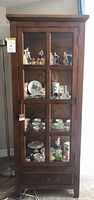 Front view of wood curio cabinet with glass panel door, interior shelves, lower drawer
