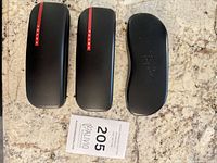 Three eyeglass cases: two Prada with red stripe, one Ray-Ban