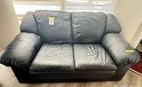 Front view of black leather loveseat showing cushions, arms and overall condition