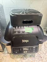 Front view Ninja Foodi Grill AG300C with detached vented top resting on lid displaying control panel and branding