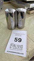 Pair of tall cylindrical stainless steel shakers standing side by side