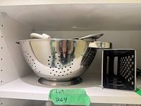 Colander, strainer, spatula, and box grater on shelf
