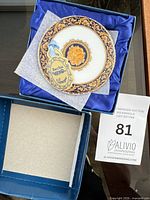 Open box showing one Bacchus coaster with tag, blue satin lining