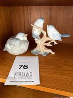 Two porcelain bird figurines on shelf with lot tag visible
