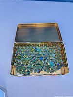 Open tin showing large quantity of marbles