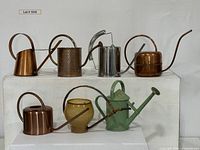 Group shot of six of the watering cans displayed on white stands
