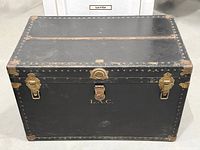front view of black steamer trunk showing hardware and initials