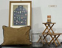 Lot overview showing framed puzzle, three stools stacked, glass jar, candle on holder, pillow