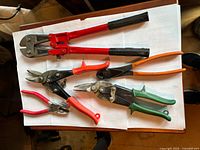 Bolt cutters, aviation snips and pliers laid out on paper