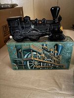 Dark amethyst glass locomotive bottle on its illustrated box