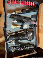 Zippered gray tool kit open showing sockets, driver bits, mini pliers, knife