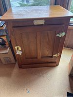 Front view of cabinet showing door, brass hinges, latch, and brand plaque