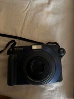 Front view of Fujifilm Instax 100 instant camera showing flash, lens and strap