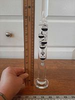 Full view of glass Galileo thermometer beside ruler showing height