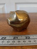 profile view of brass piggy bank with ruler showing length about 2.25 in.